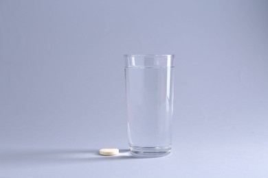Effervescent pill and glass of water on light grey background