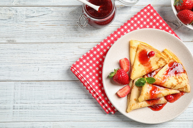 Photo of Delicious thin pancakes with strawberries and jam on white wooden table, flat lay. Space for text