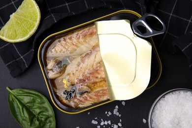 Photo of Open tin can with mackerel fillets and spices on black table, flat lay