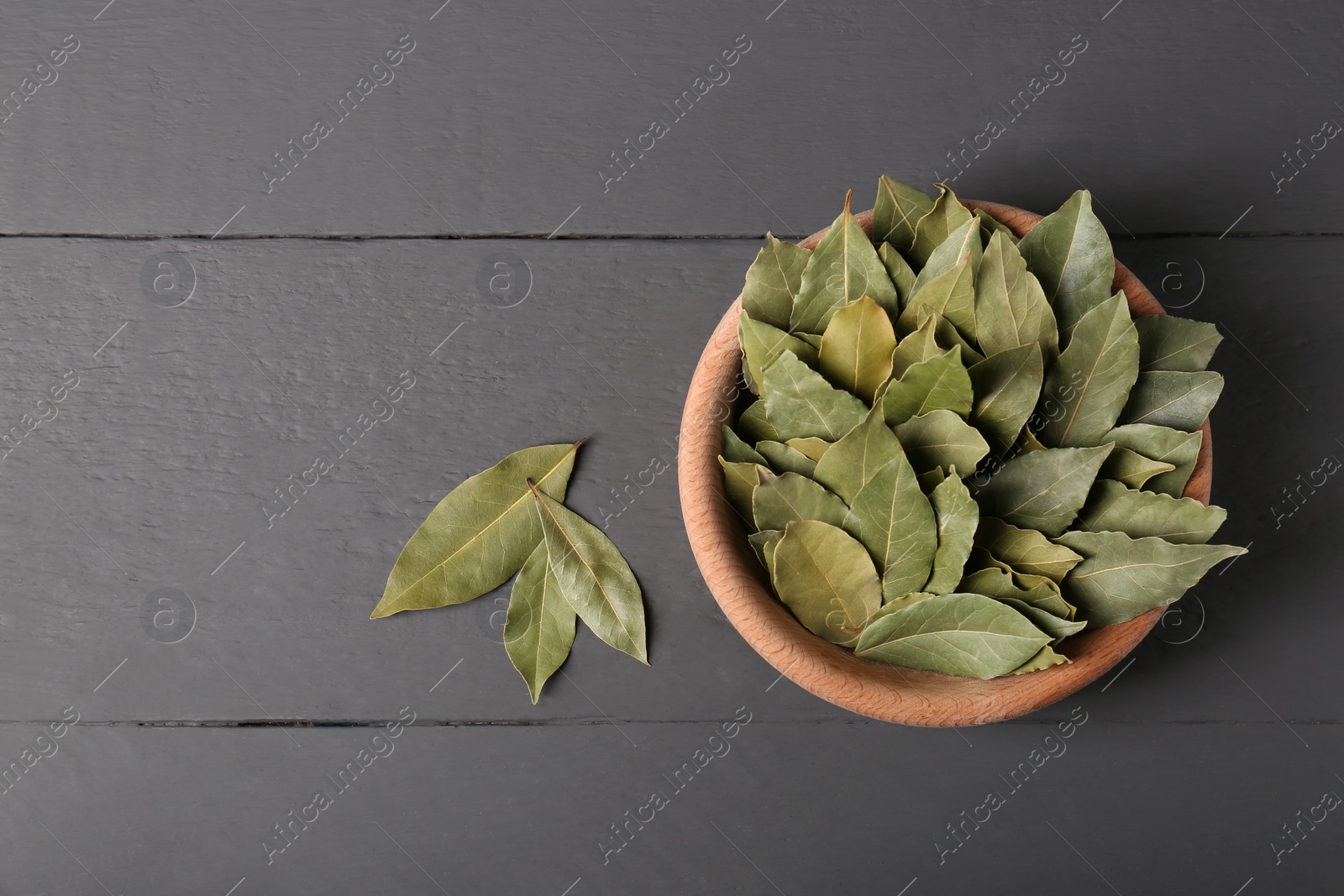 Photo of Aromatic bay leaves in wooden bowl on gray table, flat lay