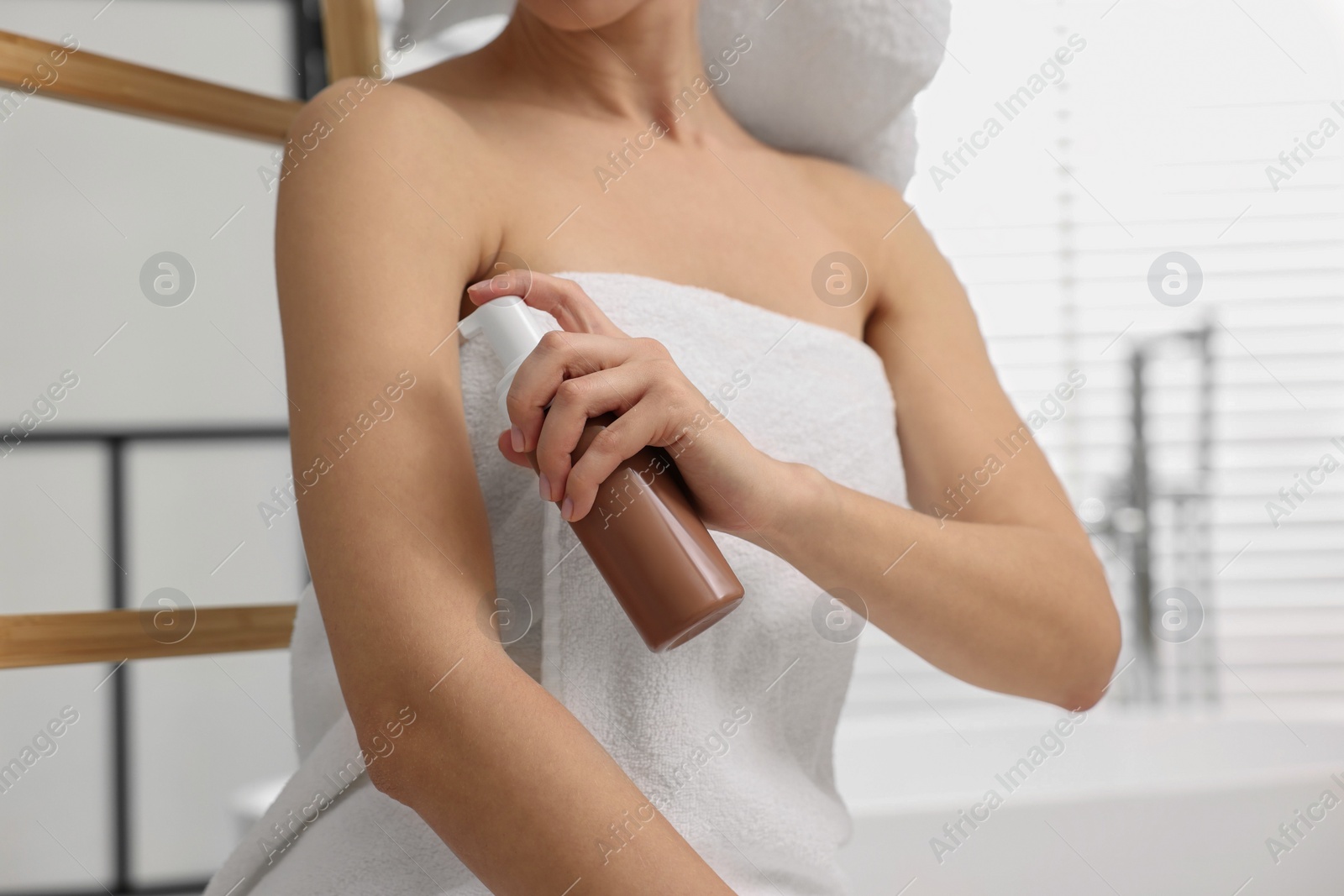 Photo of Woman applying self-tanning product onto arm in bathroom, closeup