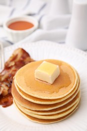 Photo of Delicious pancakes with butter, maple syrup and fried bacon on white marble table