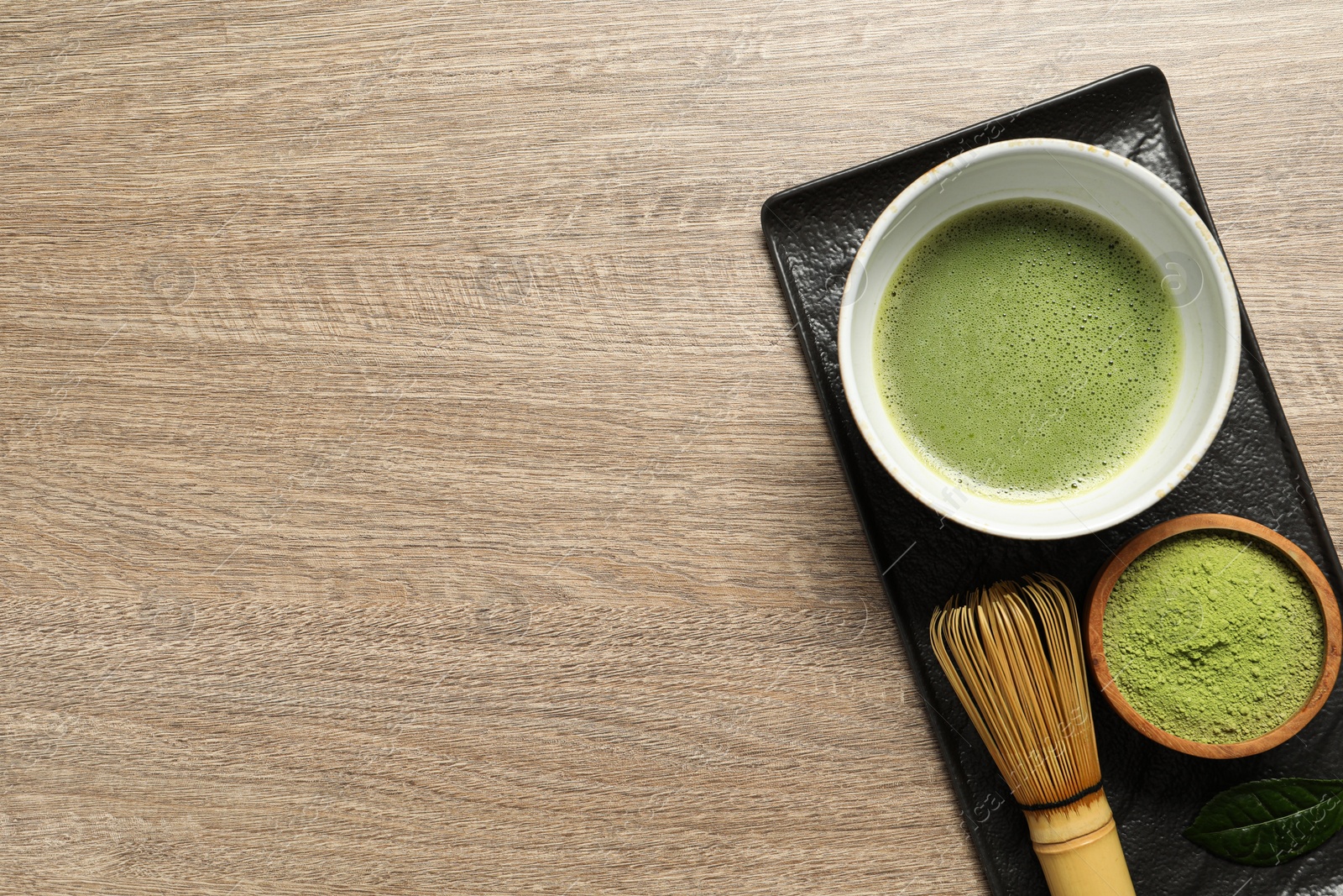 Photo of Cup of fresh matcha tea, bamboo whisk and green powder on wooden table, top view. Space for text