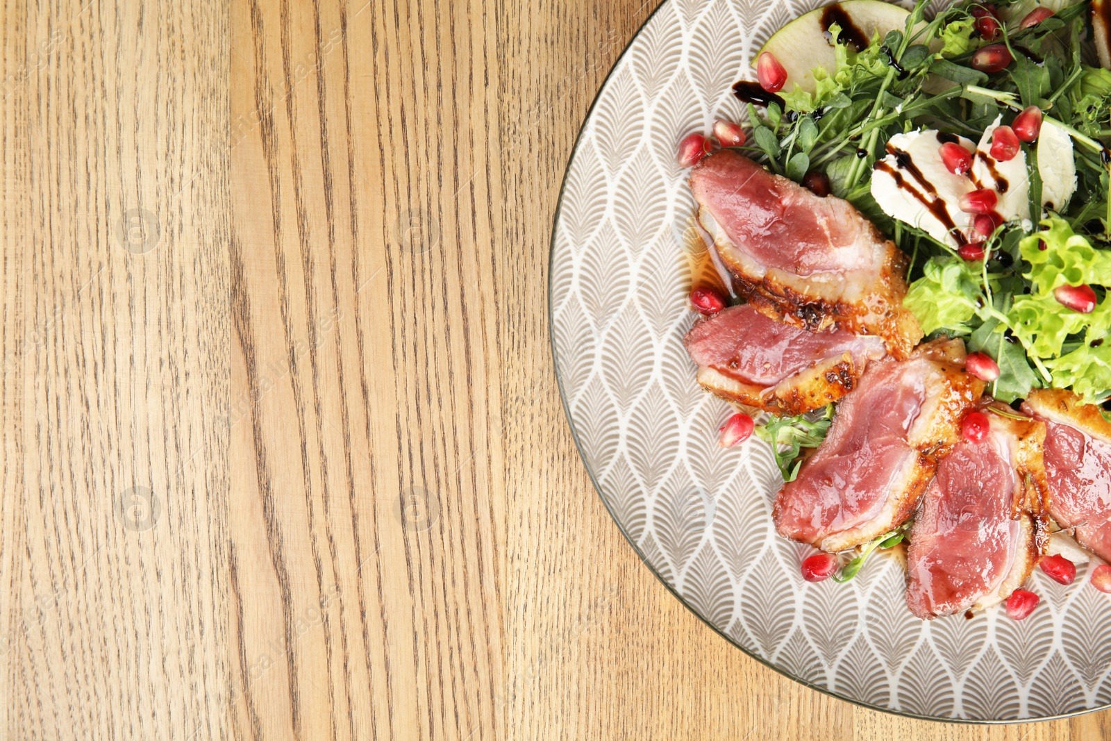 Photo of Delicious salad with roasted duck breast served on wooden table, top view. Space for text