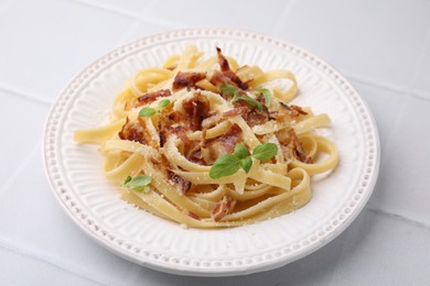 Photo of Tasty pasta with bacon and basil on white tiled table