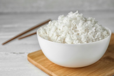 Photo of Board with boiled rice in bowl on light table. Space for text