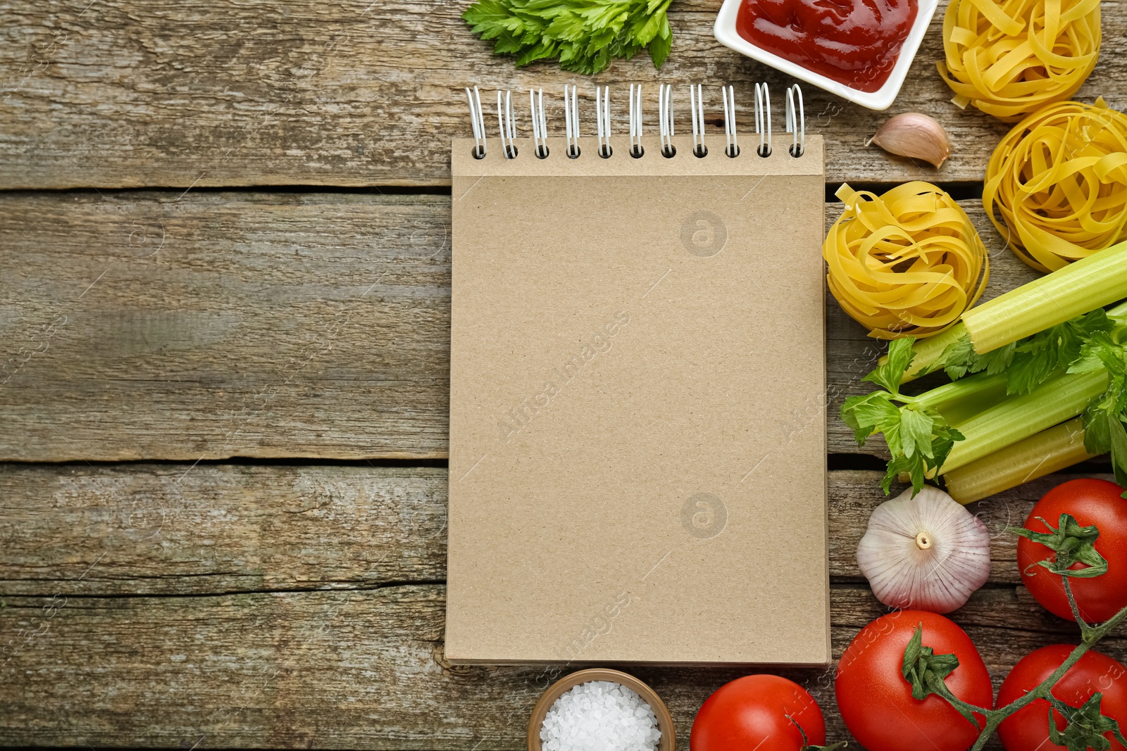 Photo of Blank recipe book and different ingredients on wooden table, flat lay. Space for text