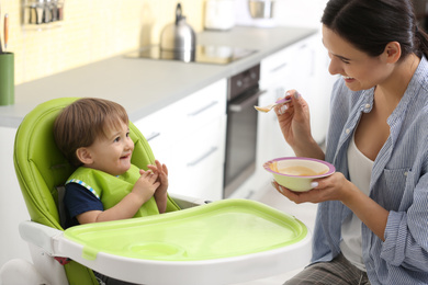 Young nanny feeding cute little baby in kitchen