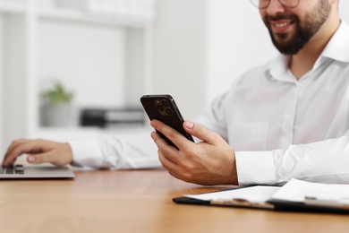 Photo of Young man using smartphone while working with laptop at wooden table in office, closeup