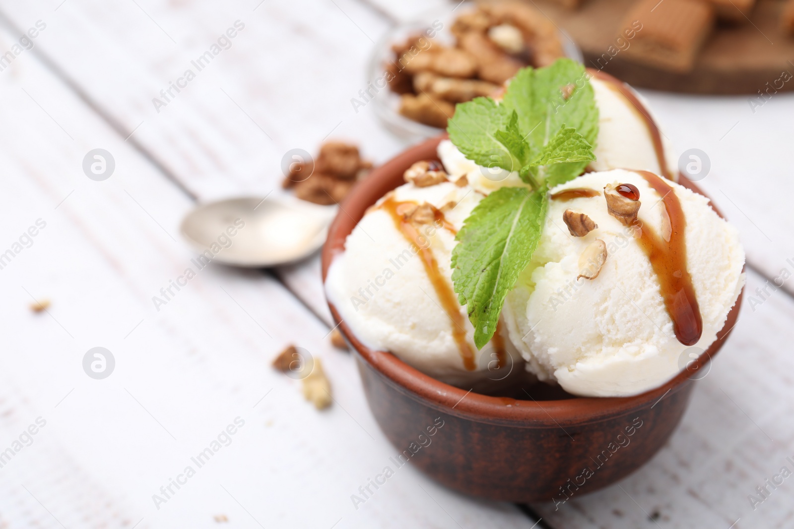 Photo of Bowl of tasty ice cream with caramel sauce, mint and nuts on white wooden table, closeup. Space for text