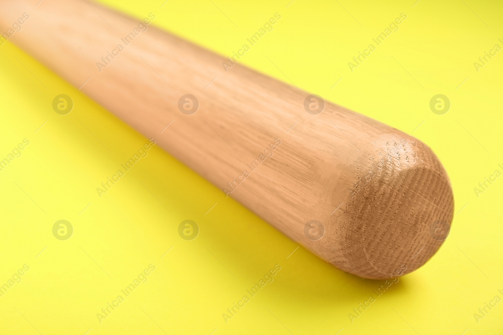 Photo of Wooden baseball bat on yellow background, closeup. Sports equipment