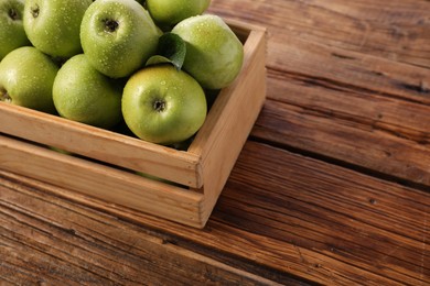 Photo of Fresh ripe green apples with water drops in crate on wooden table. Space for text