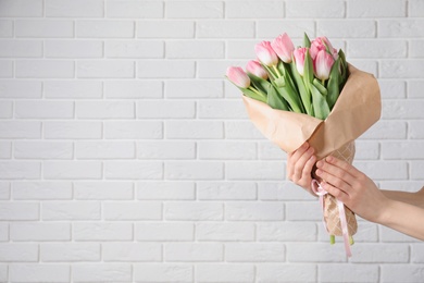 Photo of Girl holding bouquet of beautiful spring tulips near brick wall, closeup with space for text. International Women's Day