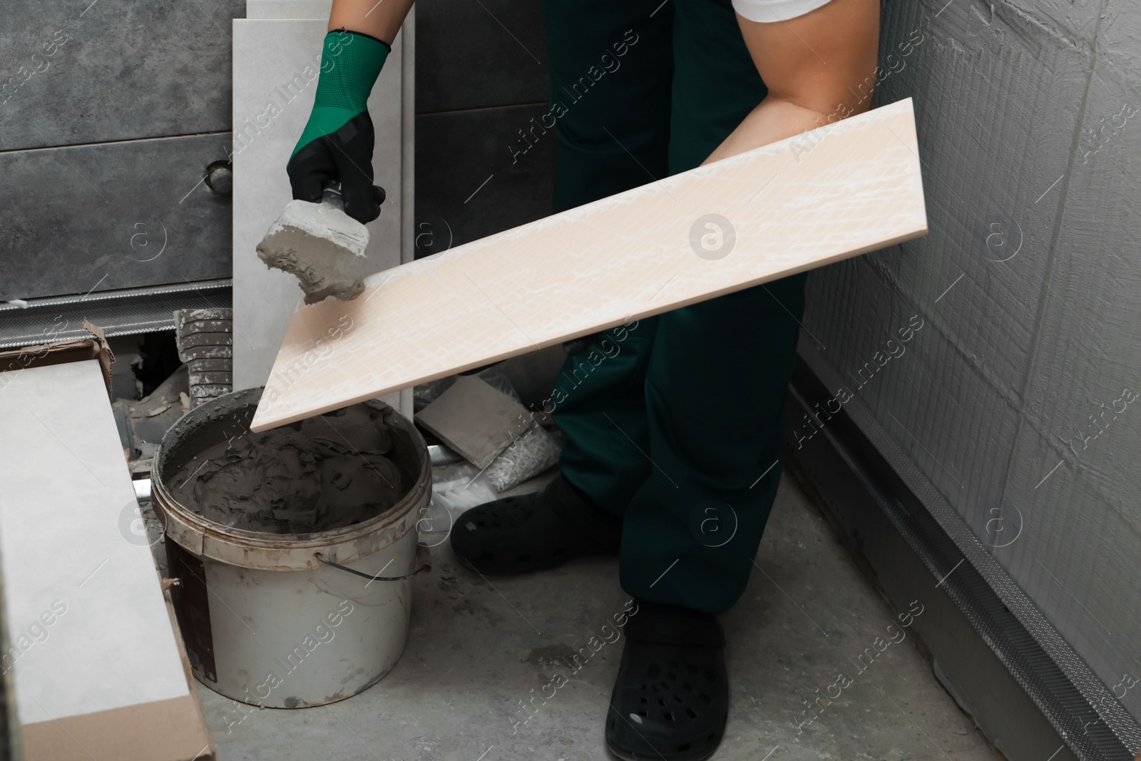 Photo of Worker applying adhesive mix on ceramic tile with spatula, closeup