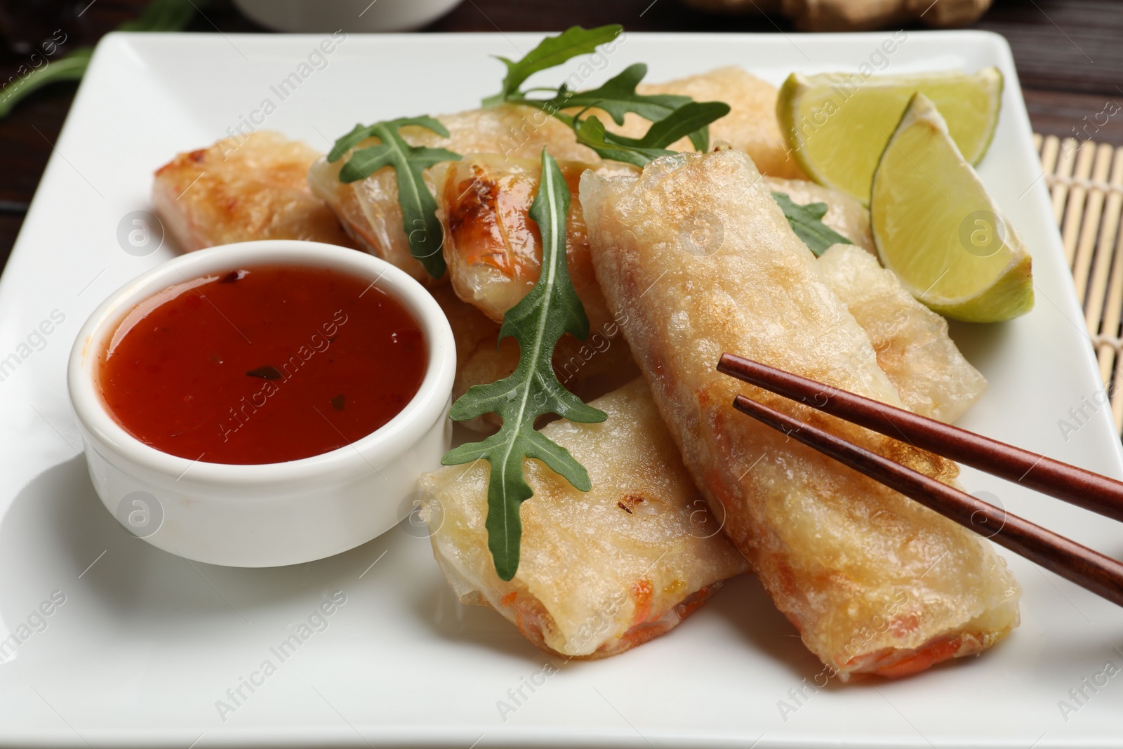 Photo of Tasty fried spring rolls, arugula, lime and sauce on table, closeup