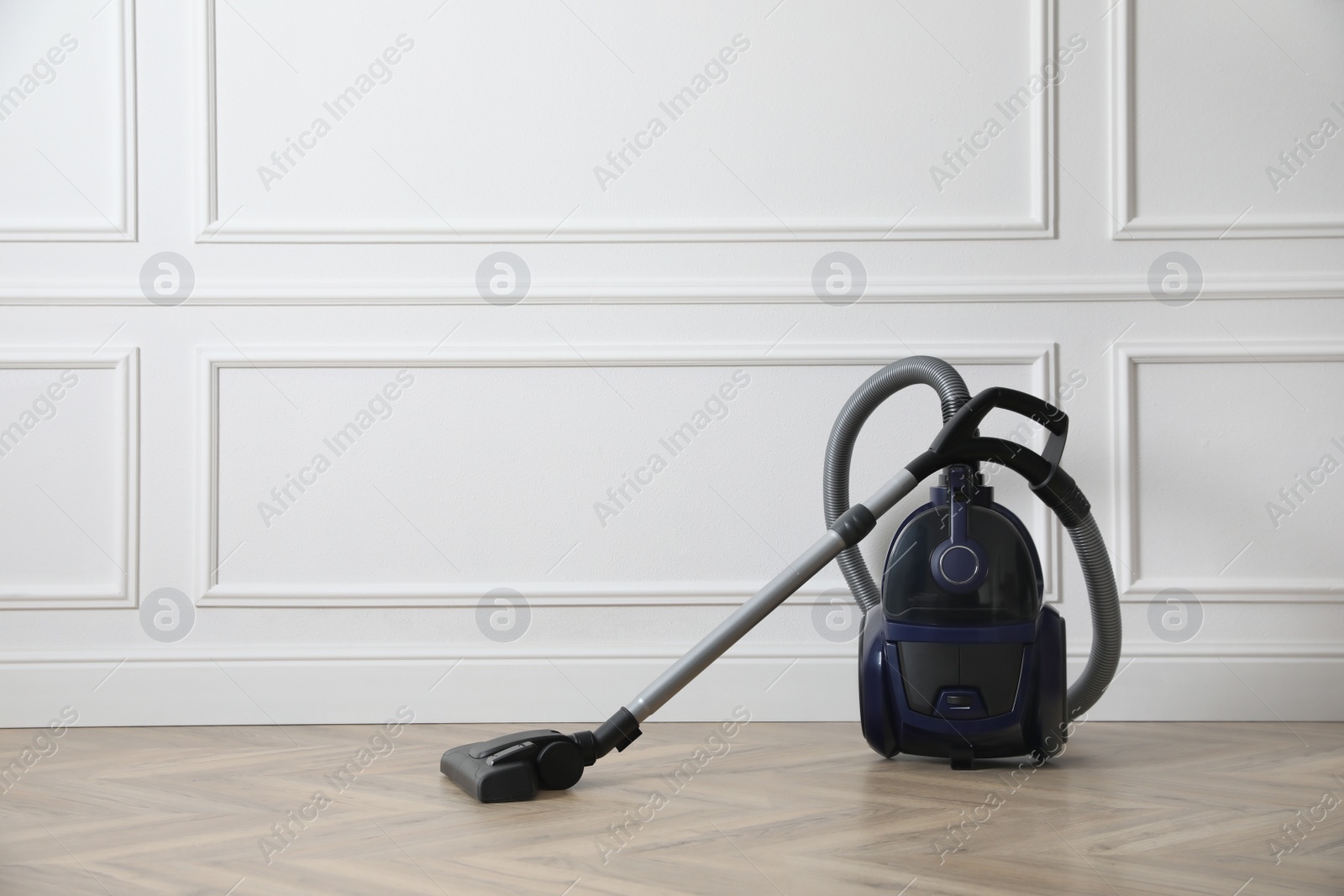 Photo of Modern vacuum cleaner near white wall indoors, space for text