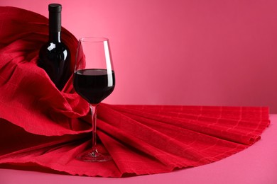 Stylish presentation of delicious red wine in bottle and glass on pink background. Space for text