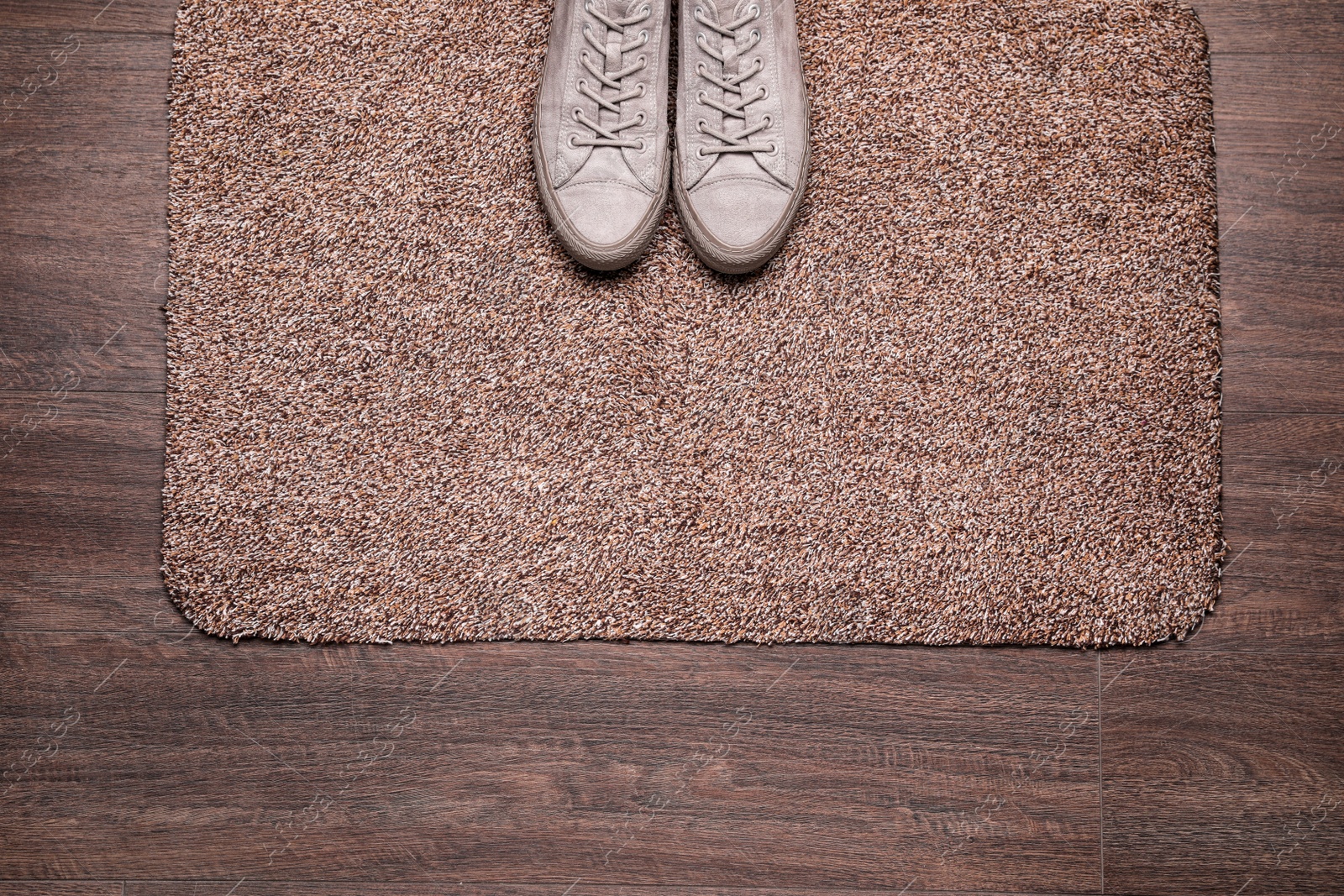 Photo of Stylish door mat and shoes on wooden floor, top view