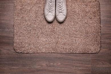 Photo of Stylish door mat and shoes on wooden floor, top view