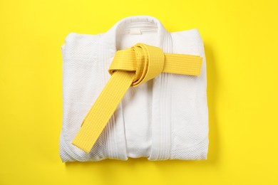 Photo of Karate belt and white kimono on yellow background, top view