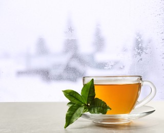 Image of Cup of hot tea on table near window covered with frost 