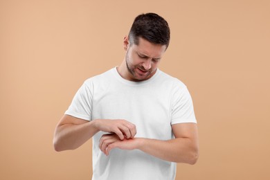 Photo of Allergy symptom. Man scratching his hand on light brown background