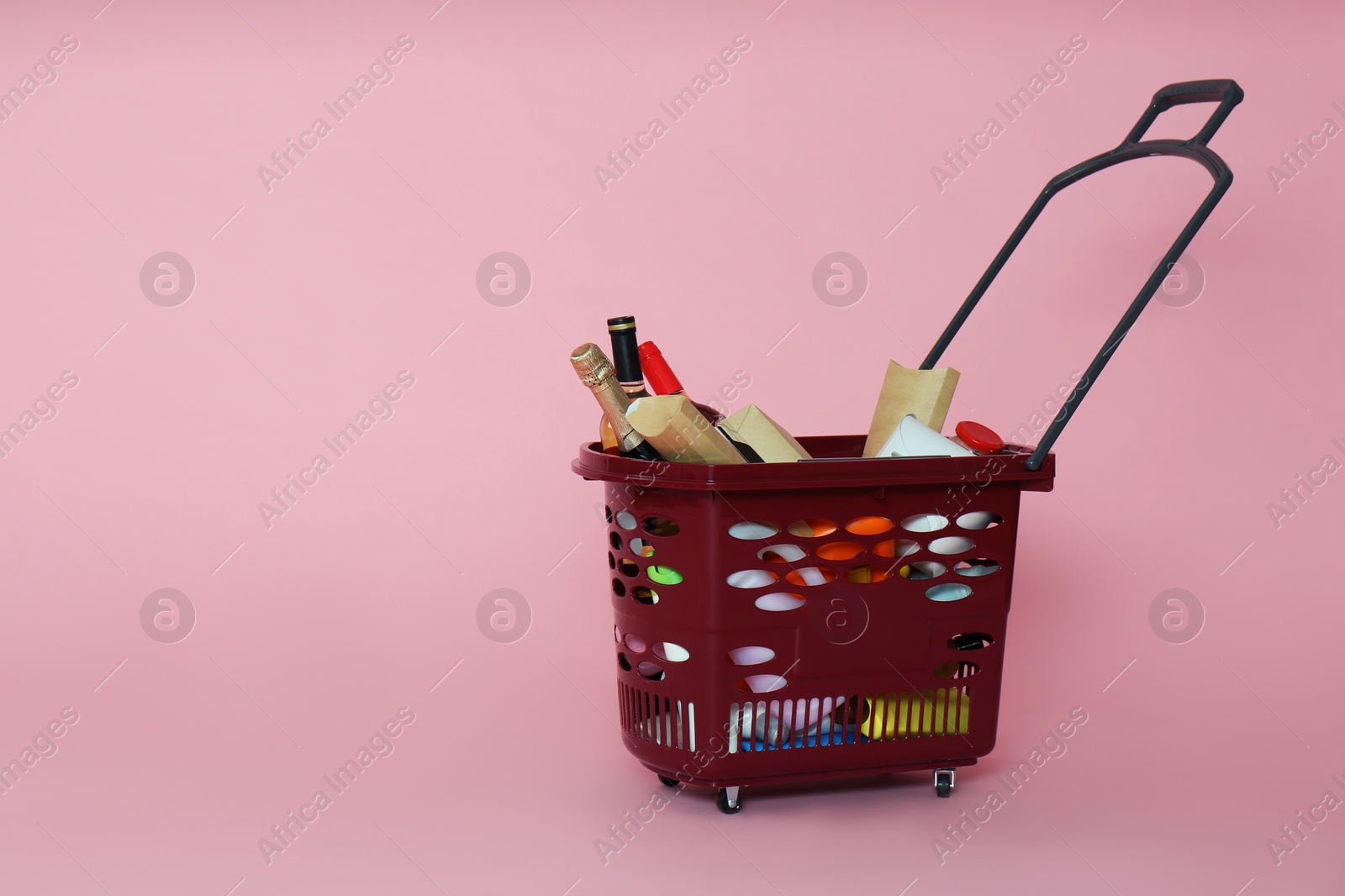 Photo of Shopping basket full of different products on pink background. Space for text