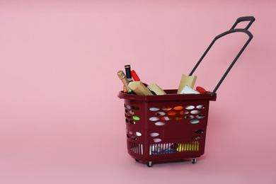 Shopping basket full of different products on pink background. Space for text