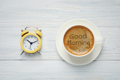 Image of Cup of aromatic coffee and alarm clock on white wooden table, flat lay. Good morning