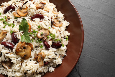 Photo of Delicious rice pilaf with mushrooms and beans on black table, closeup