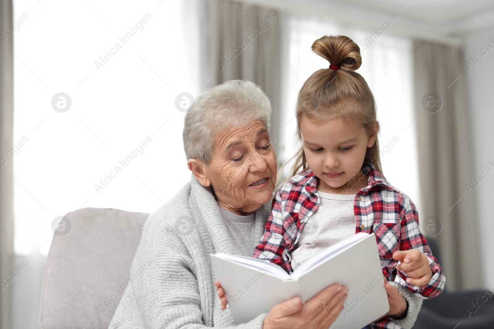 Photo of Cute girl and her grandmother reading book at home