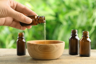 Woman pouring essential oil from glass bottle into bowl on table, closeup