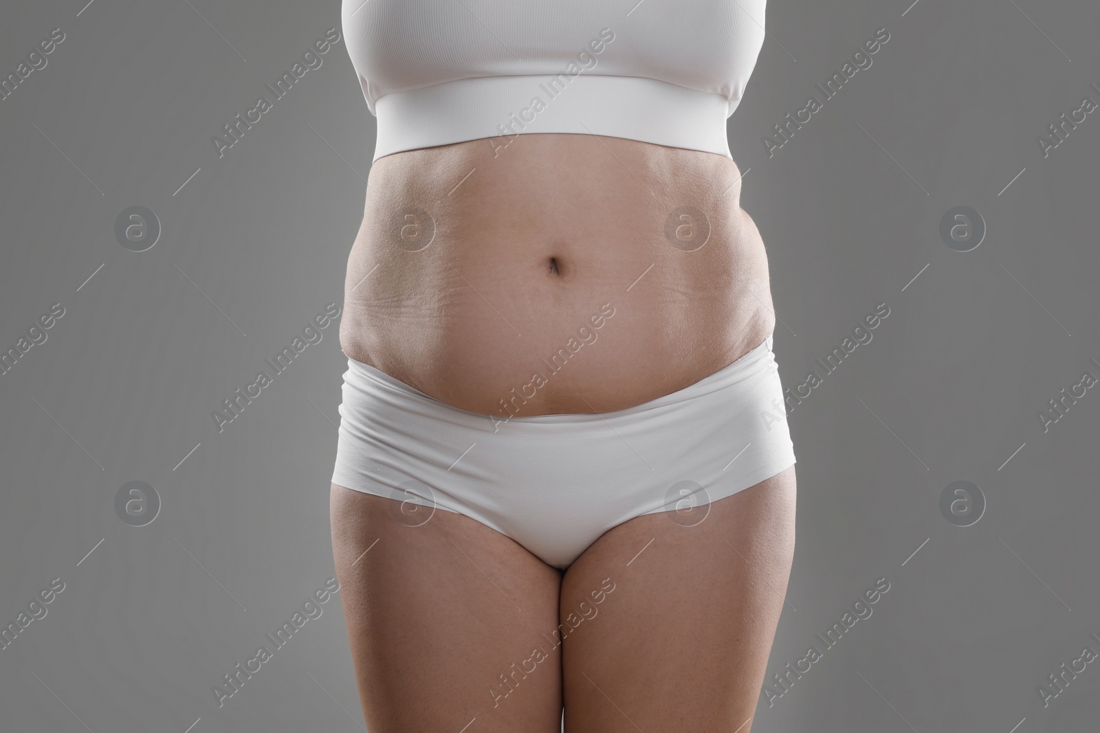 Photo of Woman with excessive belly fat on grey background, closeup. Overweight problem