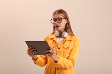 Photo of Emotional teenage student with tablet and headphones on beige background