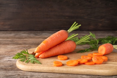 Photo of Board with cut carrot on wooden background