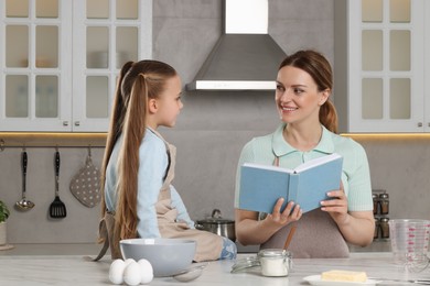 Photo of Cute little girl with her mother cooking by recipe book in kitchen