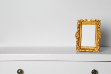 Photo of Beautiful golden vintage frame on white chest of drawers, space for text
