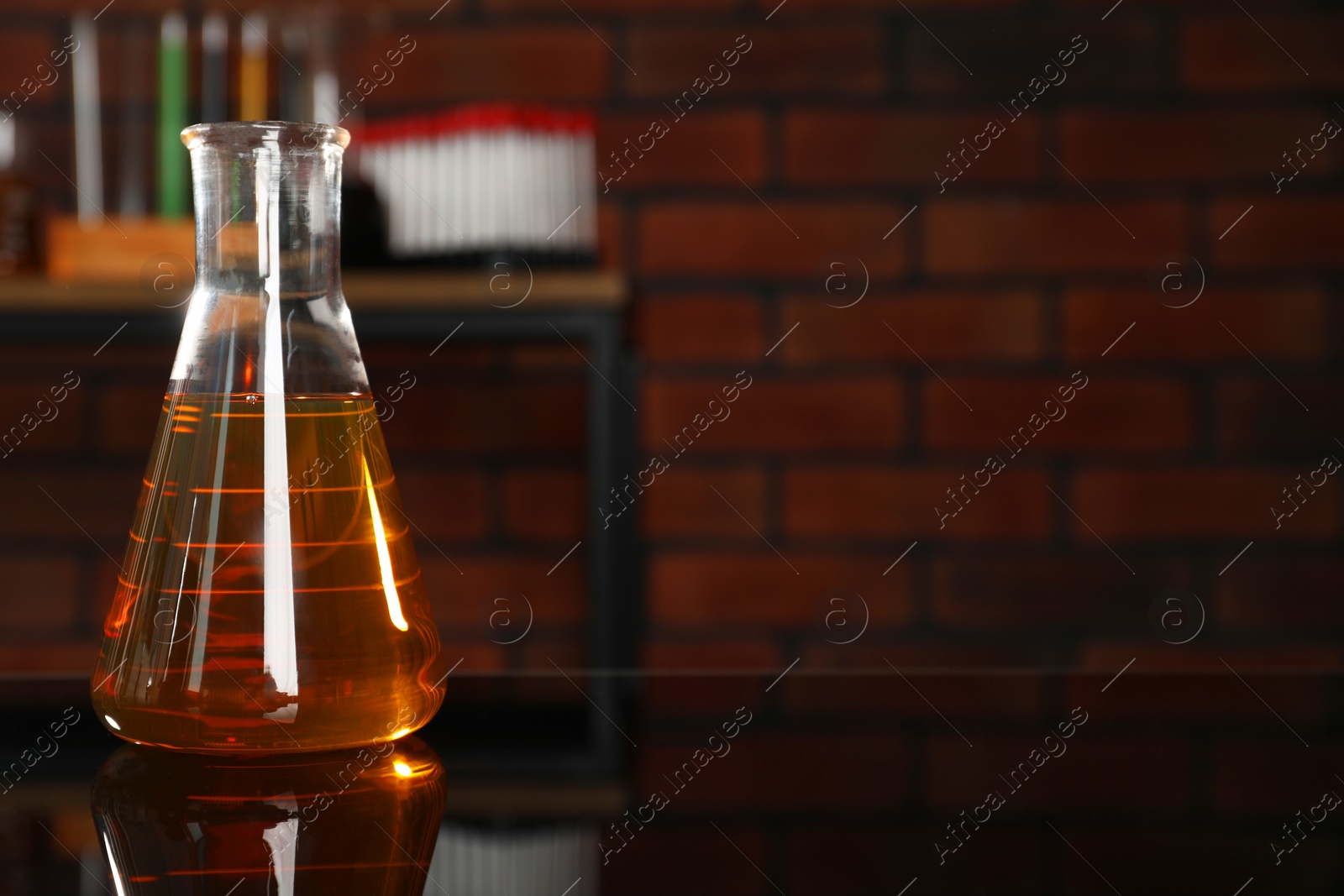 Photo of Flask with yellow oil on black mirror table indoors, closeup. Space for text