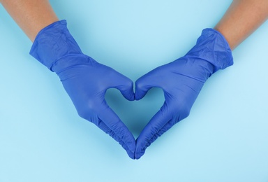 Photo of Person in medical gloves making heart with hands on light blue background, top view