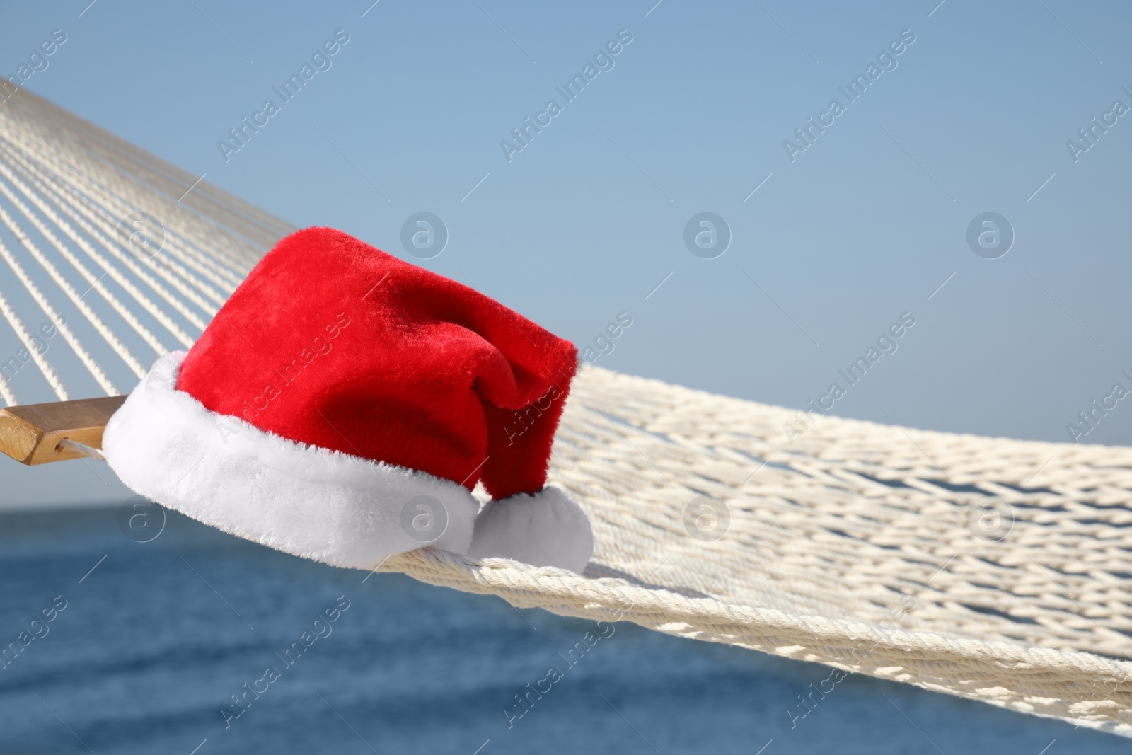 Photo of Rope hammock with Santa's hat on beach, closeup. Christmas vacation