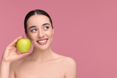 Beautiful young woman with apple on pink background. Space for text