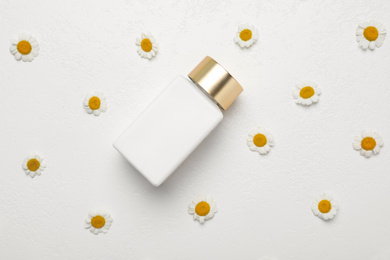 Flat lay composition with chamomile flowers and cosmetic product on white background