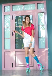 Happy girl with retro roller skates standing near pink door