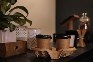 Photo of Takeaway coffee cups with cardboard holder on wooden table indoors