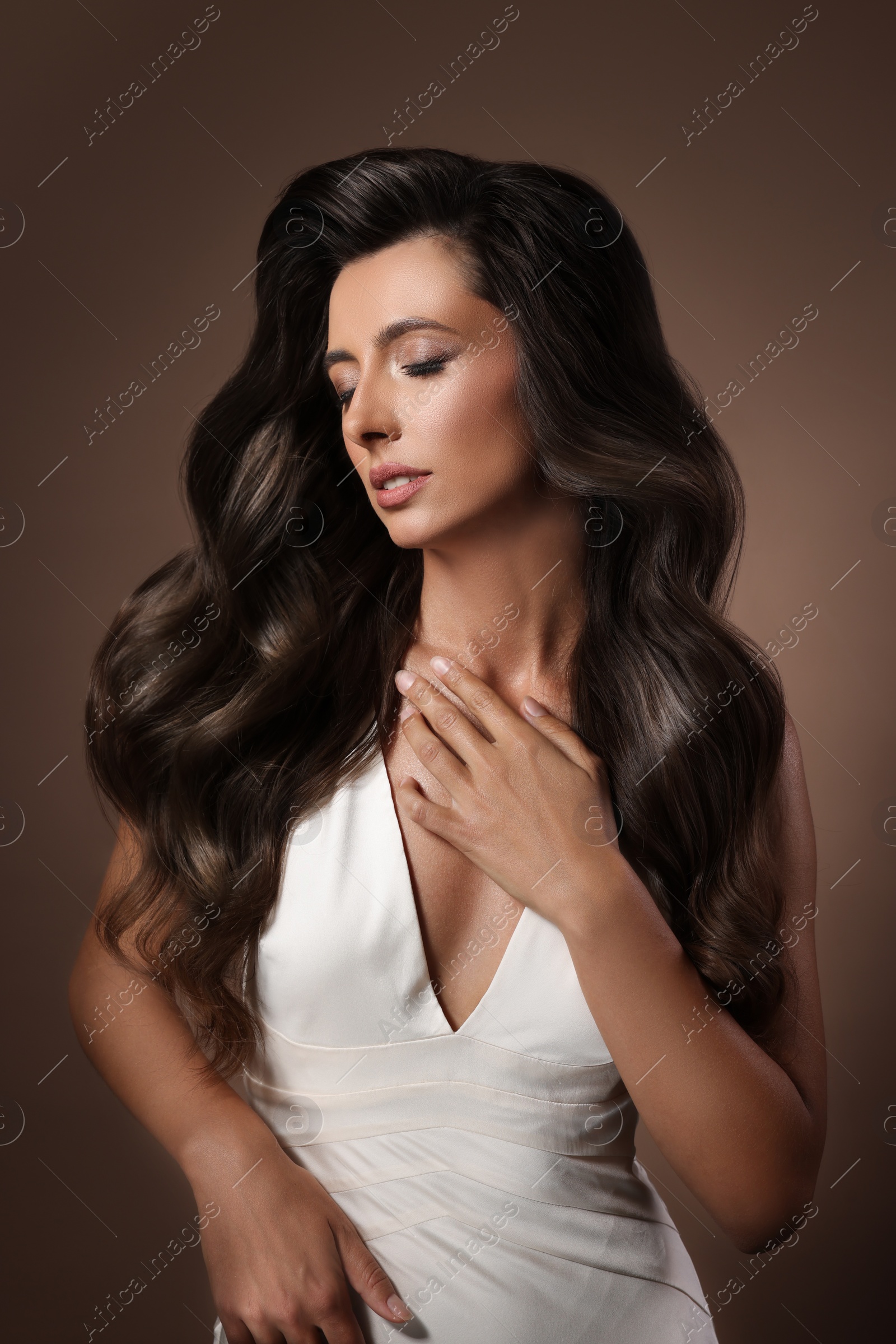 Image of Gorgeous woman with shiny wavy hair on brown background. Professional hairstyling