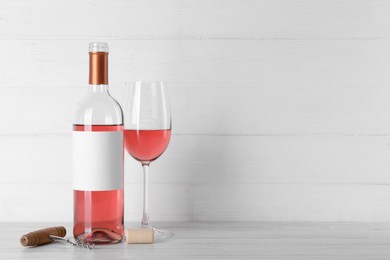 Photo of Corkscrew near bottle and glass of delicious rose wine on table against white wooden background. Space for text