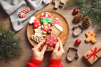 Woman holding tasty homemade Christmas cookie over wooden table, top view
