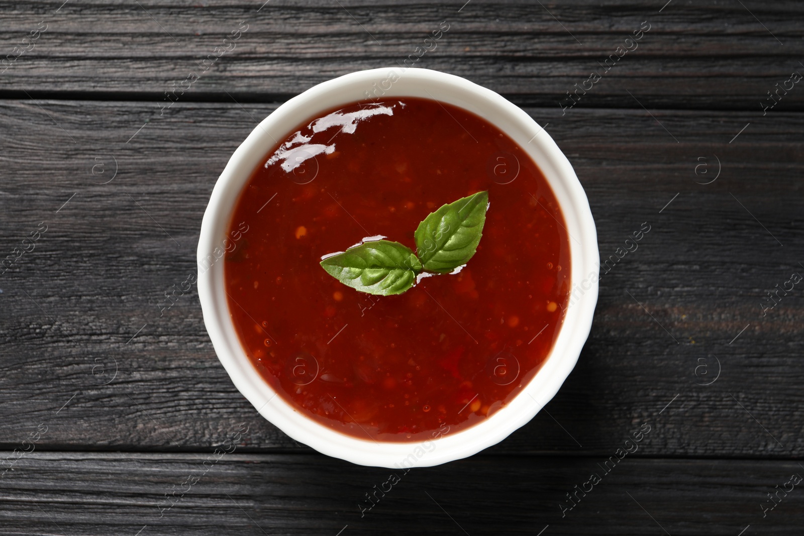 Photo of Spicy chili sauce with basil on dark wooden table, top view