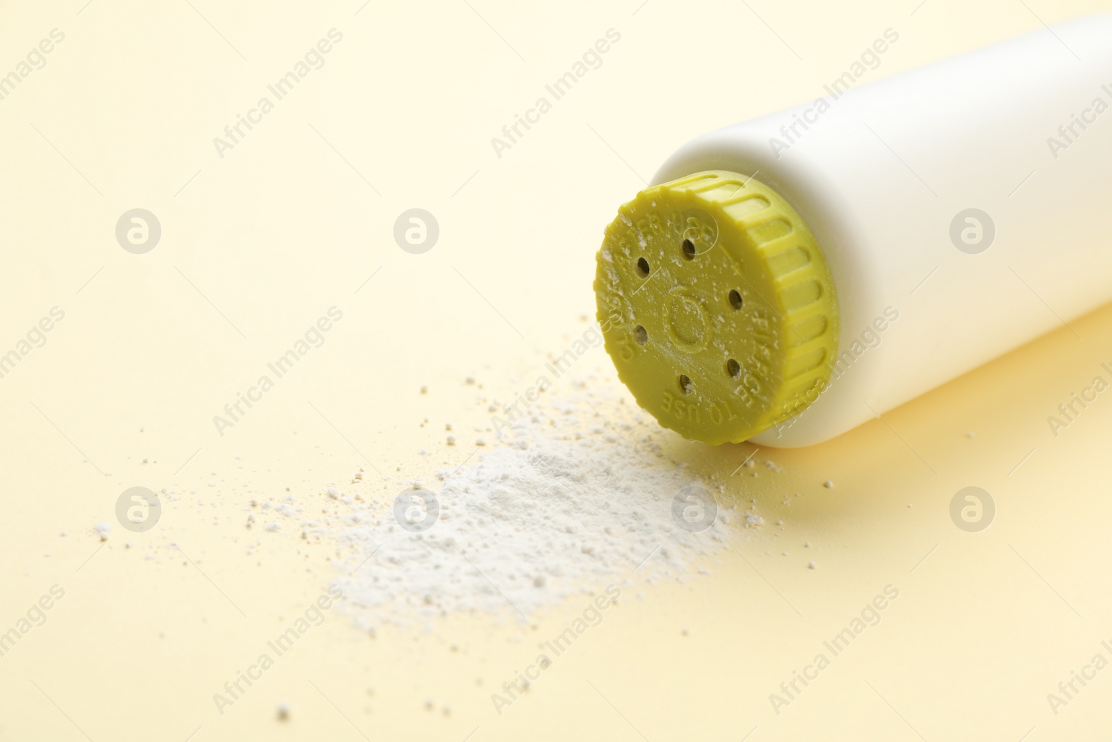 Photo of Bottle and scattered dusting powder on beige background, closeup. Baby cosmetic product