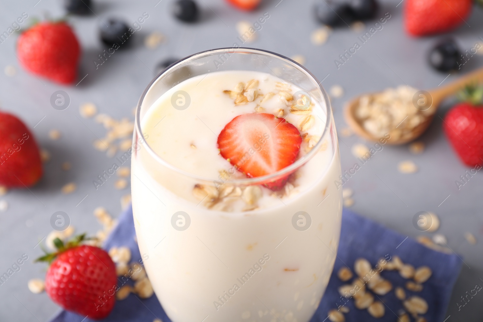 Photo of Tasty yogurt in glass, oats and berries on grey table, closeup